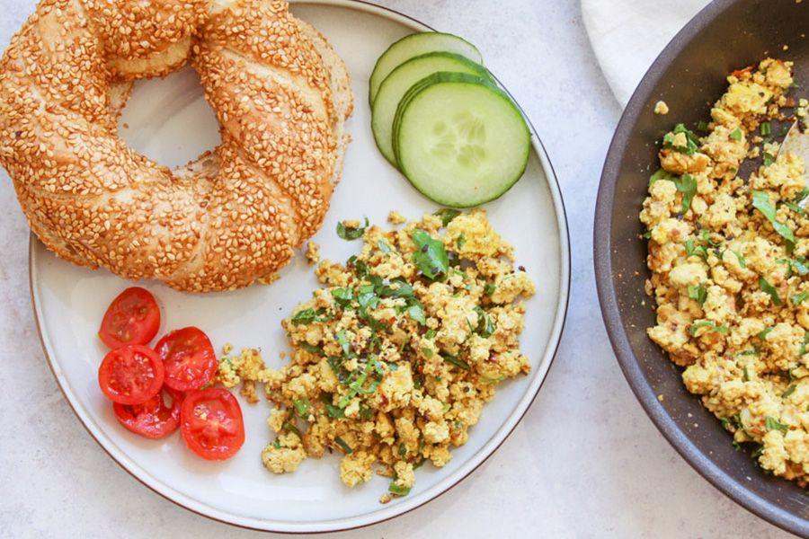 Frühstücksteller mit Bagel, veganem Rührei und Rohkost.