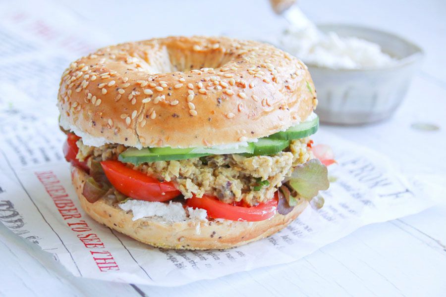 Bagel belegt mit veganem Aufstrich, Tomaten, grünem Salat, veganem Thunfisch aus Kichererbsen und Gurkenscheiben.